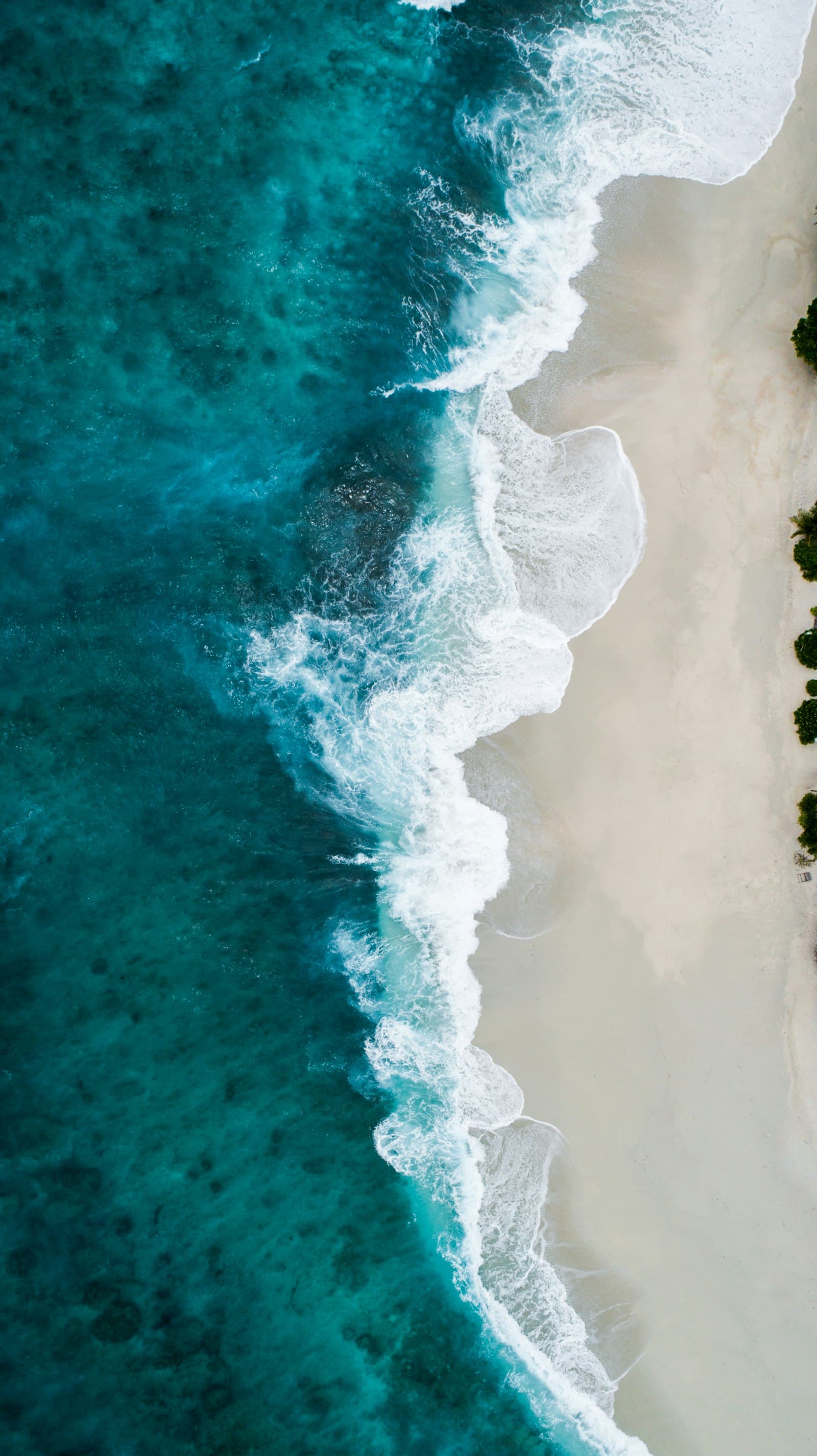 Aerial view of turquoise waves meeting a white sand beach