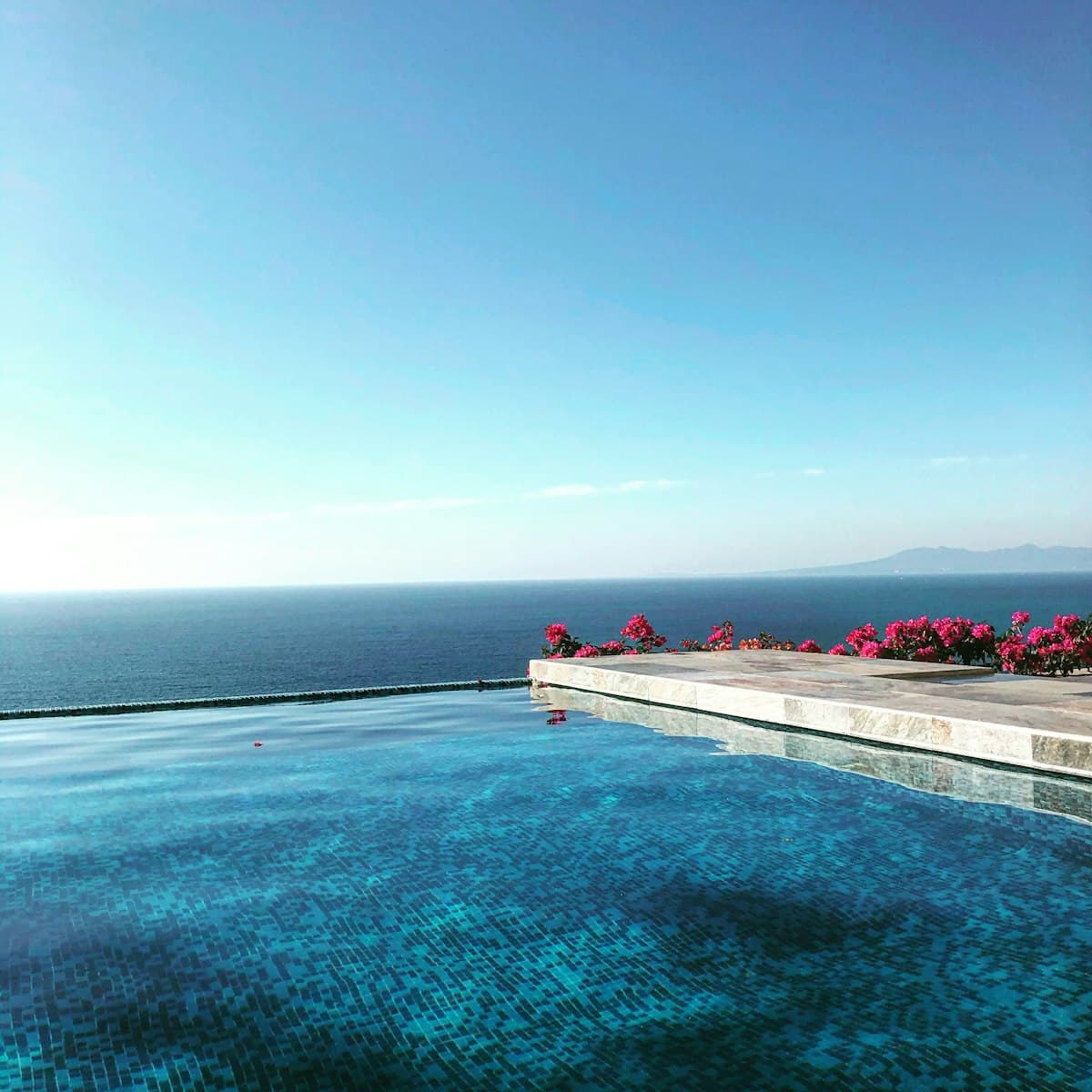 Vivid turquoise infinity pool on a cliff edge framed by bougainvillea