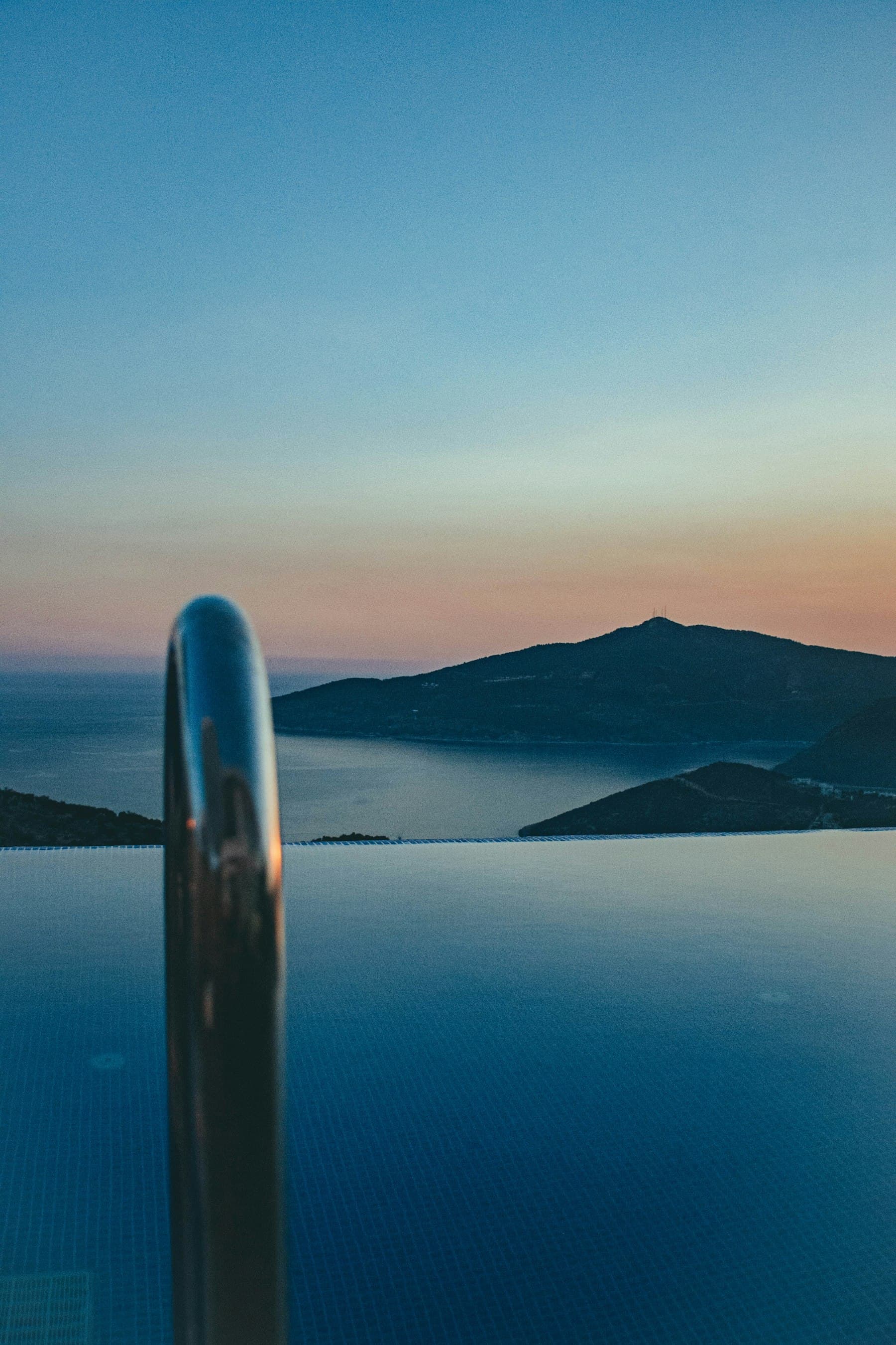 Infinity pool at dusk overlooking a mountain silhouette and the sea